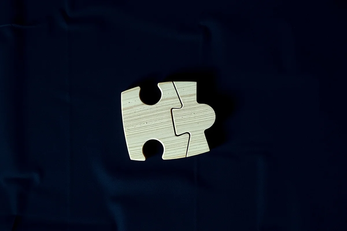 due tessere di puzzle in legno chiaro incastrate tra loro, viste dall'alto su un tessuto blu scuro